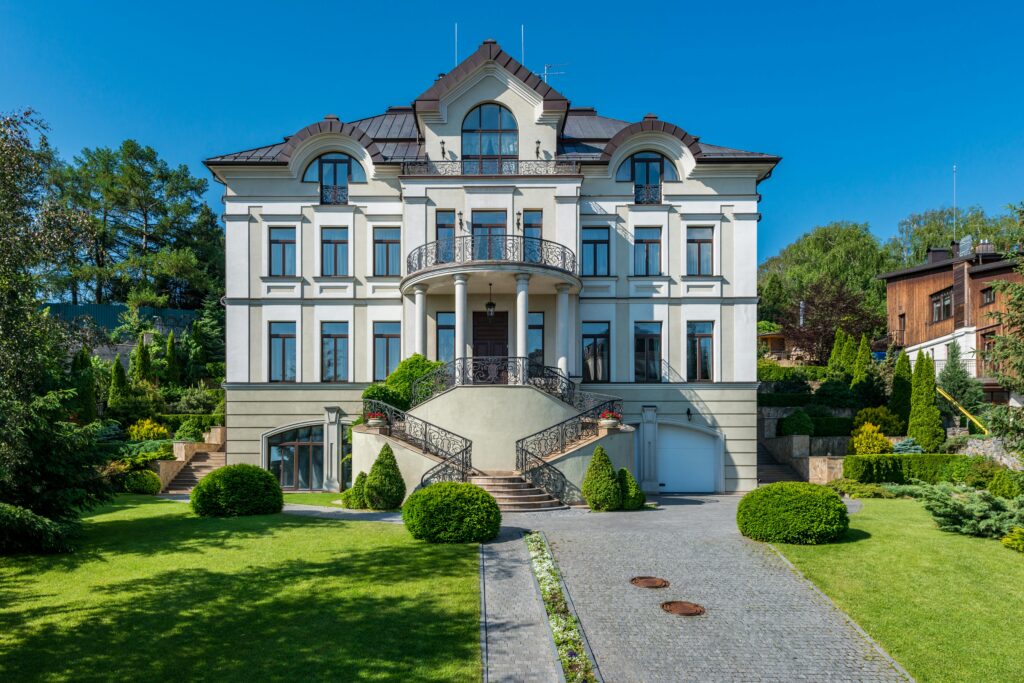 Ventes A luxurious mansion surrounded by a lush, manicured garden under a clear blue sky.
