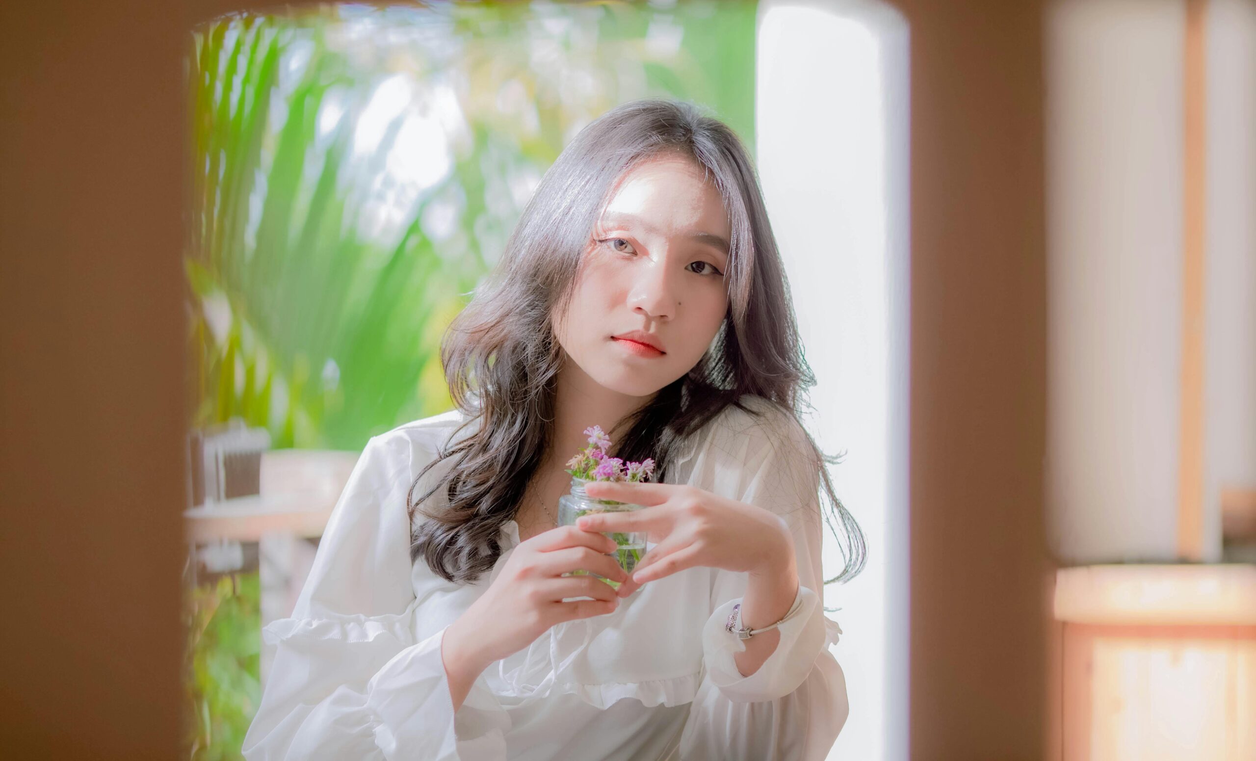 A serene portrait of a woman with black hair holding flowers in natural light.