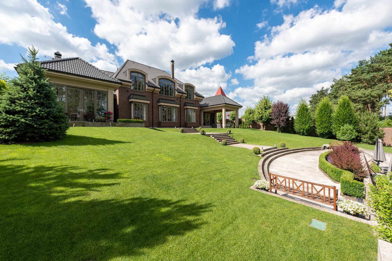 services-02 Elegant brick mansion with manicured lawn and garden under a bright blue sky.